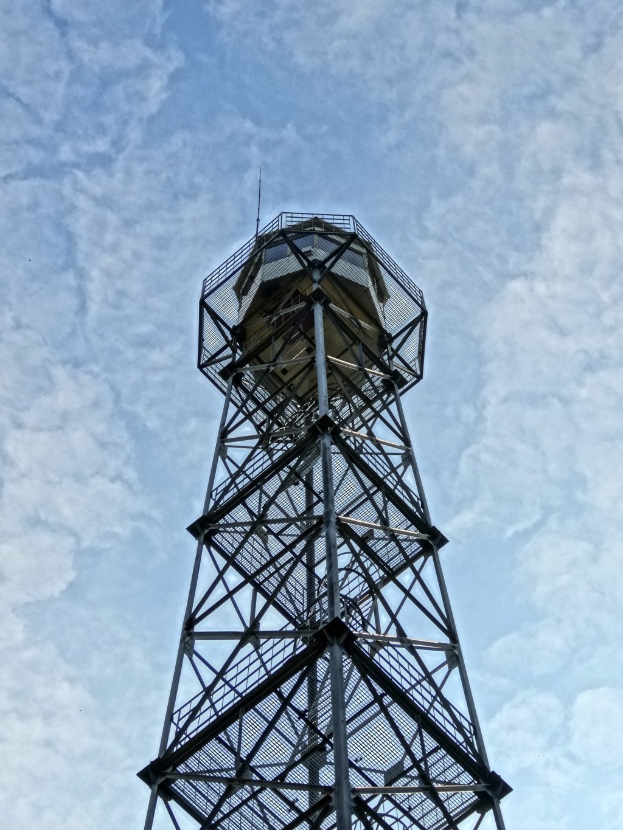 Ein hoher Metallfeuerturm vor einem blauen Himmel mit weißen Wolken.