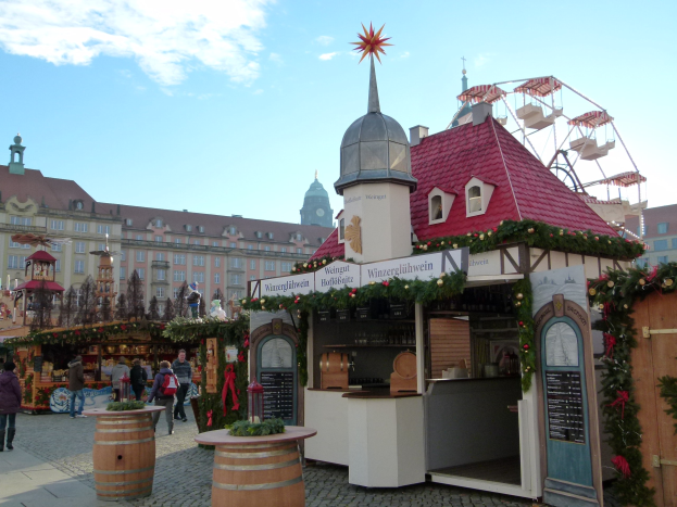 Ein geschäftiger Weihnachtsmarkt in Nürnberg, Deutschland, mit Menschen um geschmückte Stände, festliche Lichter, Schmuck, Gebäude mit Fenstern, ein Riesenrad und einen bewölkten Himmel, mit einer Tafel mit Text auf der rechten Seite.