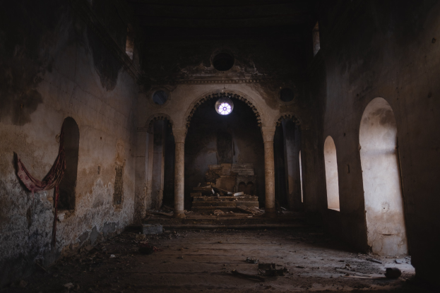 Alter Bau mit Bögen und Säulen, mit einem drapierten Tuch an der linken Wand, verstreuten Bodenobjekten und einem zentralen Fenster, das eine verlassene Kirche mit dunkler Atmosphäre vermittelt.