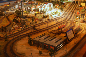 Eine detaillierte Miniatur-Modellbahnausstellung in einem Museum, die Gebäude, Bäume, Schienen, Fahrzeuge und urbane Elemente umfasst, die eine belebte Stadtlandschaft nachahmen.