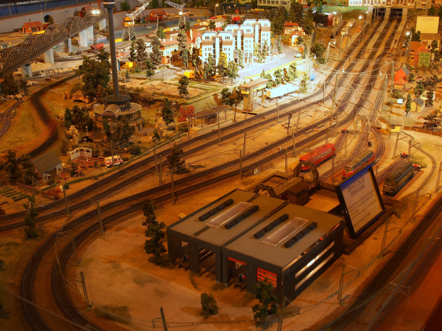 Eine detaillierte Miniatur-Modellbahnausstellung in einem Museum, die Gebäude, Bäume, Schienen, Fahrzeuge und urbane Elemente umfasst, die eine belebte Stadtlandschaft nachahmen.