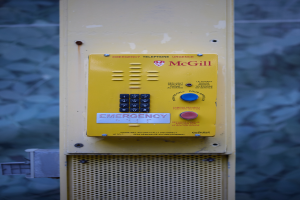 Ein gelber Notrufhörer an einer Gebäudeseite angebracht, mit Tasten und Text für Notrufe.