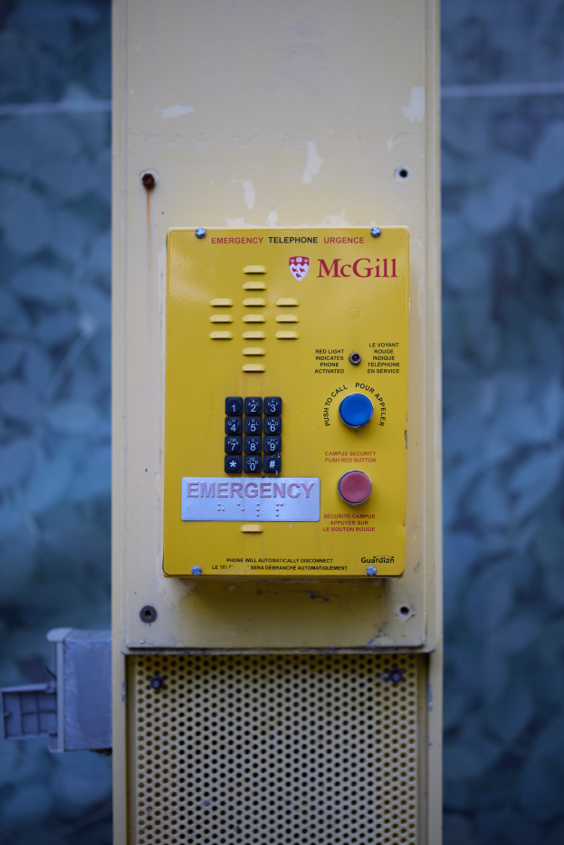 Ein gelber Notrufhörer an einer Gebäudeseite angebracht, mit Tasten und Text für Notrufe.