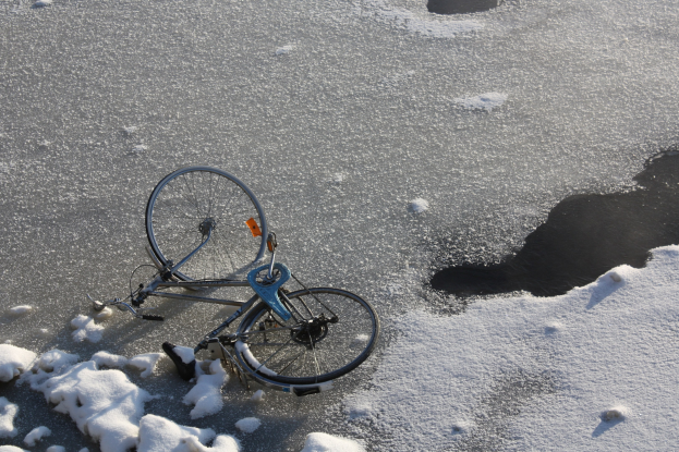 Ein Fahrrad liegt im Schnee neben einer Pfütze, mit Schnee bedecktem Boden.