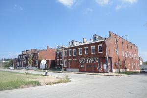 Ein Gebäude mit Masten und Straßenlaternen, umgeben von Bäumen und Fahrzeugen auf beiden Seiten, mit einem Weg, Gras und einem Feuerlöscher unten und dem Himmel oben.