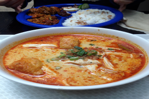 Eine Person steht vor einem Tisch mit einem Tablett, das Schüsseln mit Speisen enthält.