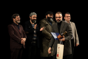 Eine Gruppe von Männern steht auf einer Bühne bei Nacht, einer hölt eine Tasche und eine Trophäe, und feiert die Eröffnung der Berliner Filmfestspiele.