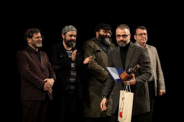 Eine Gruppe von Männern steht auf einer Bühne bei Nacht, einer hölt eine Tasche und eine Trophäe, und feiert die Eröffnung der Berliner Filmfestspiele.