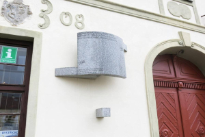 Ein Gebäude mit einer roten Tür und einem Schild, das ein Glasfenster mit einer Tafel zeigt, die "Szczecin City Hall" auf der linken Seite trägt, und eine Wand mit Text und einer Skulptur.
