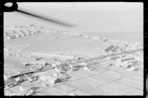 Eine Schwarz-Weiß-Aufnahme einer Kleinstadt mit zahlreichen Häusern und umliegender Landschaft.