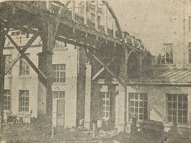 Altes Schwarz-Weiß-Foto eines Gebäudes im Bau mit sichtbaren Fenstern, Säulen und Himmel, beschriftet mit 'Bau einer Eisenbahnbrücke in den 1890er Jahren' unten.