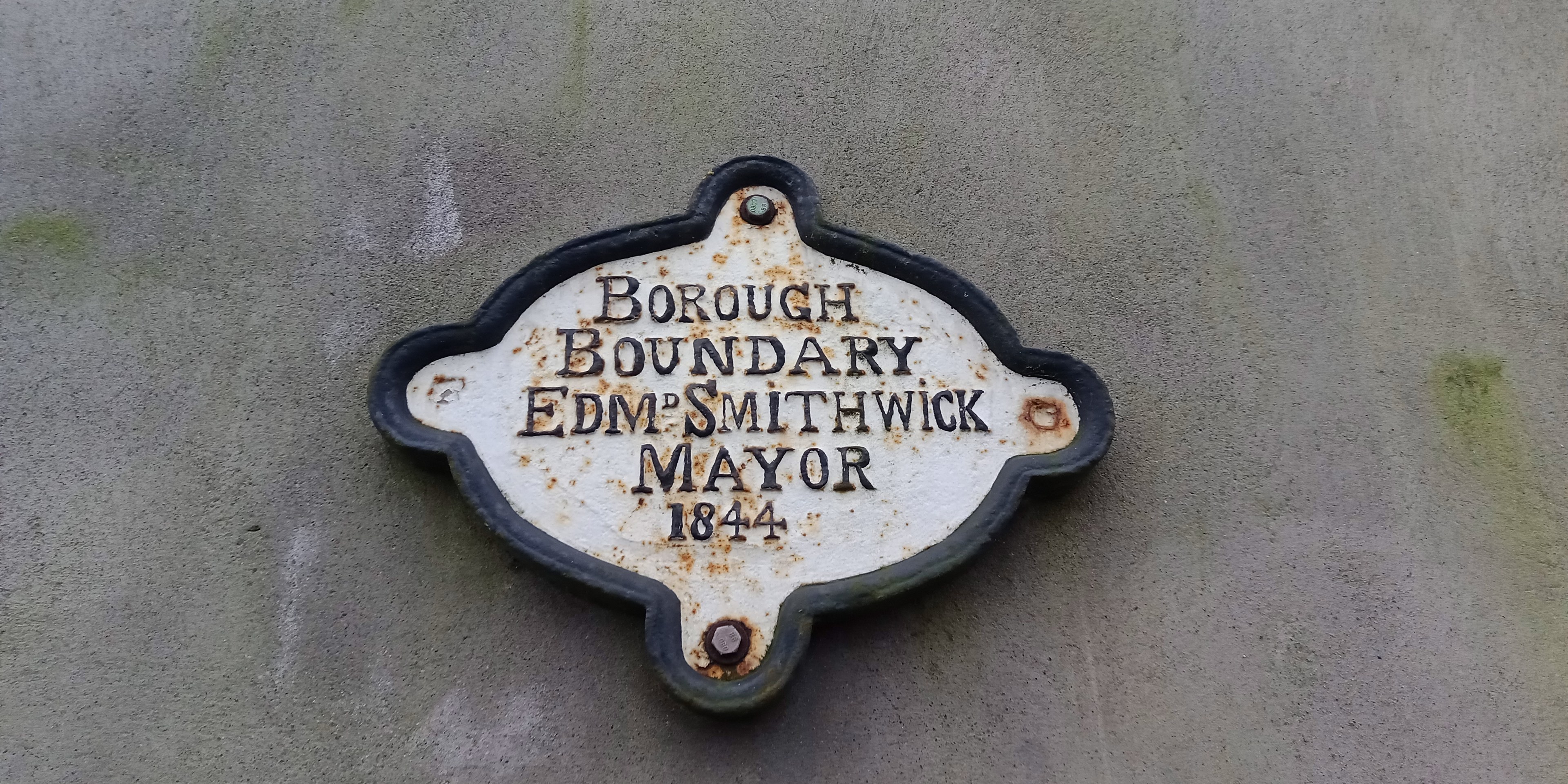 Plakette an der Gebäudeseite, die die Borough-Grenze markiert, mit "Edm Smithwick Mayor" in weißer fettgedruckter Schrift auf einem schwarzen Metallhintergrund.