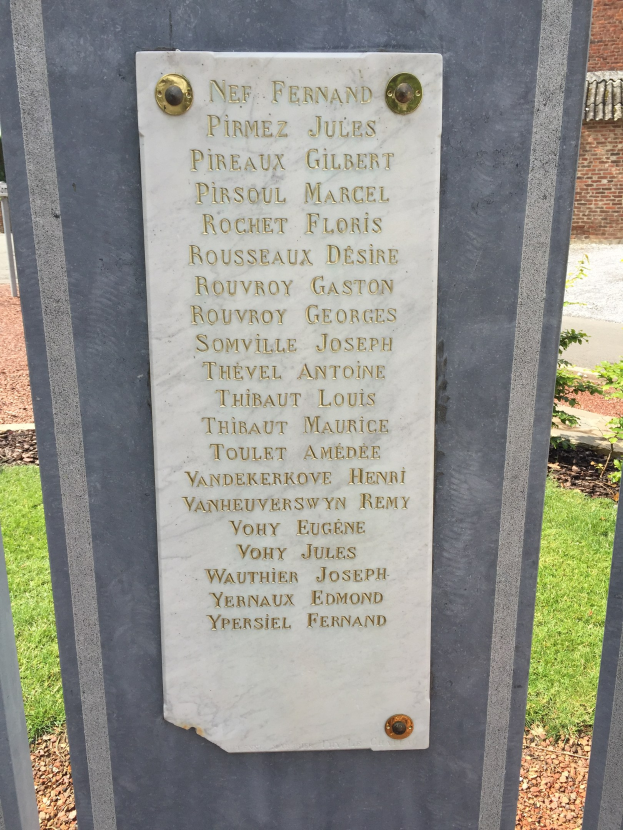 Steinbank mit Gedenktafel vor einem Backsteingebäude, umgeben von Grün.