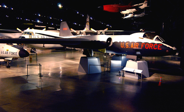 Eine Gruppe von Kampfflugzeugen in einem dunklen Museum ausgestellt, umgeben von St├Ąnden, Verkehrskegeln und anderen Bodenobjekten.