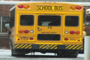 Ein gelber Schulbus parkt vor einem Backsteingebäude mit Fenstern.