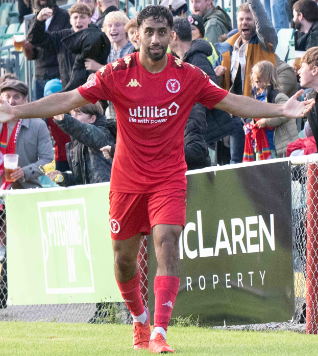 Ein Fußballer in roter Uniform rennt mit ausgebreiteten Armen auf einem Feld, mit einer Menge im Hintergrund und einem Banner mit der Aufschrift "Middlesbrough FC v Swansea City - Sky Bet Championship" im Vordergrund.