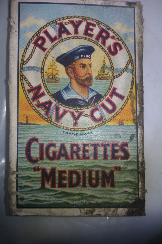 Plakat, das "Player's Navy Cut Cigarettes Medium" bewirbt, zeigt eine Person in einer marineblauen Uniform mit weißem Hemd und roter Krawatte, die Arme verschränkt und einen strengen Gesichtsausdruck hat, mit fetter schwarzer Schrift auf einem weißen Rand.