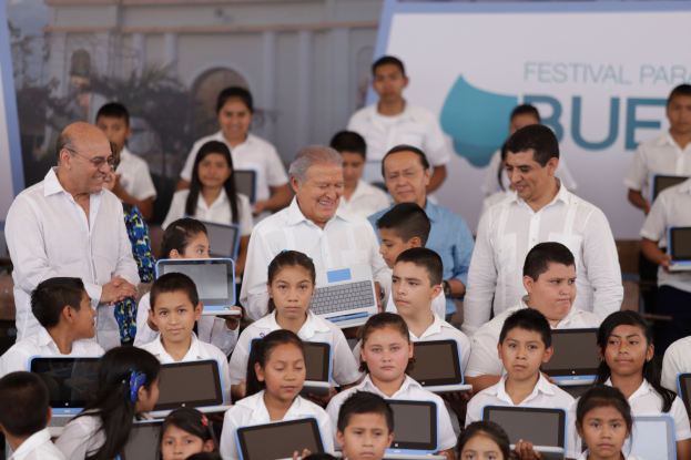 Eine Gruppe von Kindern sitzt vor einer Menschenmenge mit Laptops, im Hintergrund eine Wand mit der Aufschrift "Festival Paraiso Blue".