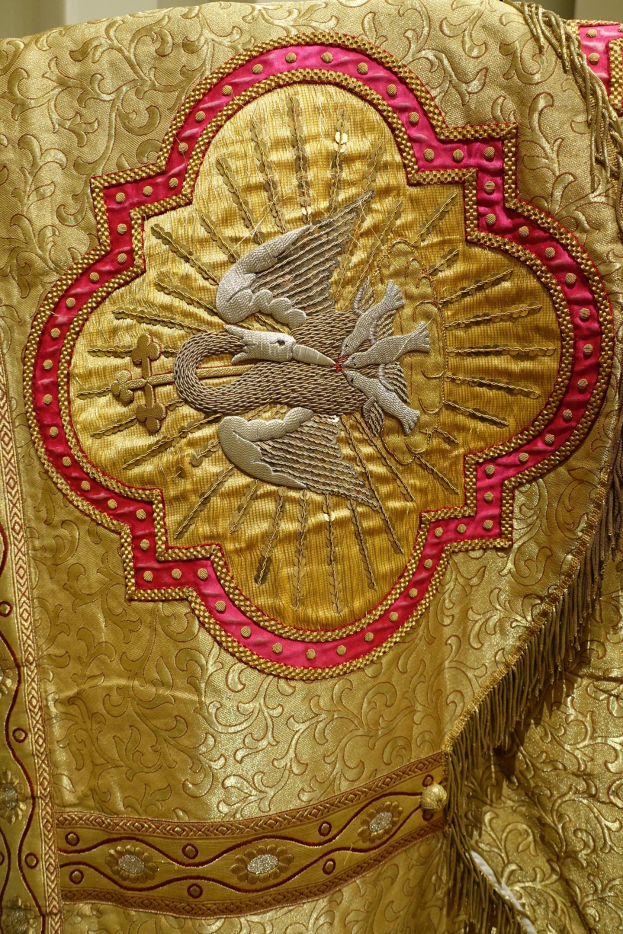 Nahaufnahme eines Priestergewandes mit aufwendiger Gold- und Roterie gegen eine Wand im Hintergrund.