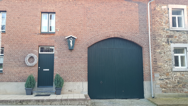 Ein Ziegelgebäude mit einer grünen Tür und Fenstern, einer Leitung an der Seite und Topfpflanzen davor.