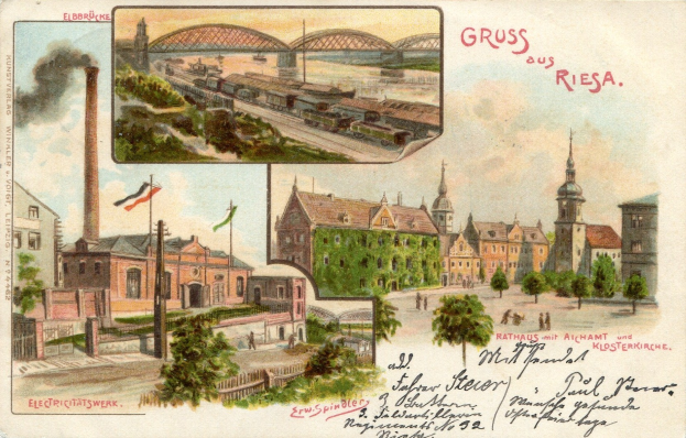 Alte Ansichtskarte mit einer Stadtansicht mit Gebäuden, Bäumen, Strommasten, Fahnen, einer Brücke, einem rauchenden Zug auf Schienen und einem Himmel, mit handgeschriebener Schrift auf der Vorderseite.