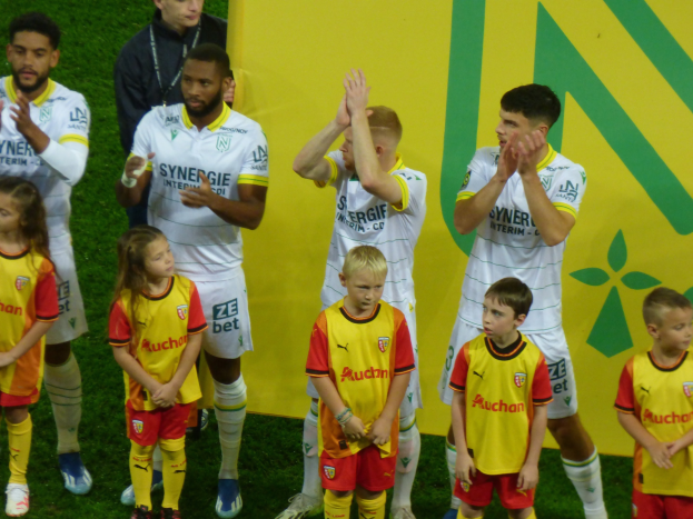 Eine Gruppe von Fußballspielern in Uniformen klatscht im Jubel auf einem Ligue 1-Feld, wobei "Ligue 1" im Hintergrund sichtbar ist.