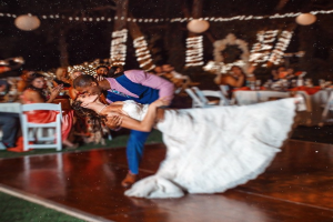 Eine Person küsst eine Frau, während andere an Tischen mit dekorativen Bällen, Bäumen und Lichtern im Hintergrund sitzen.