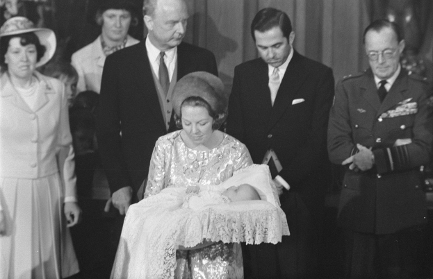 Königin Elizabeth II. wiegt ihren neugeborenen Sohn Prinz Philip, während Prinz Philip, Herzog von Edinburgh, neben ihr in einem Anzug und Krawatte steht, mit Vorhängen im Hintergrund.