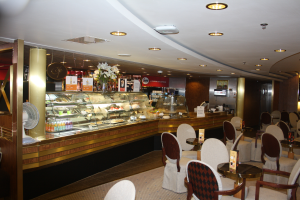 Ein Restaurant-Innenraum mit Tischen und Stühlen, einer Theke mit Blumenvasen, Texttafeln, einem Ventilator und anderen Gegenständen unter einer Decke, die mit warmem Licht beleuchtet ist.