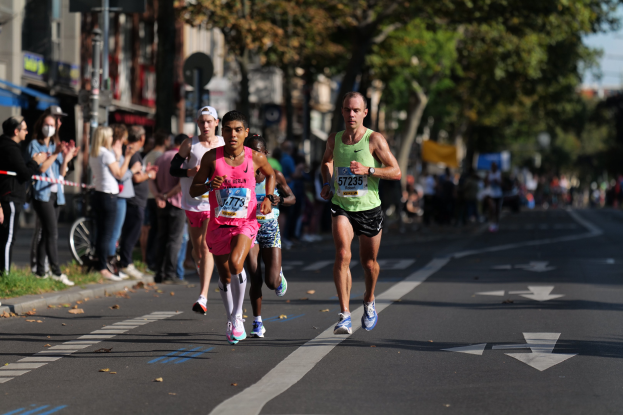 Eine Gruppe von Läufern, die an einem Marathon auf einer Stadtstraße teilnehmen, mit Zuschauern auf der linken Seite der Straße.