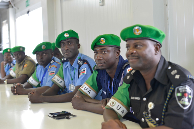 Gruppe von Polizisten an einem Tisch während einer Schulung, mit Mobiltelefonen und anderen Gegenständen auf dem Tisch, in einem Raum mit Fenstern und Deckenbeleuchtung.