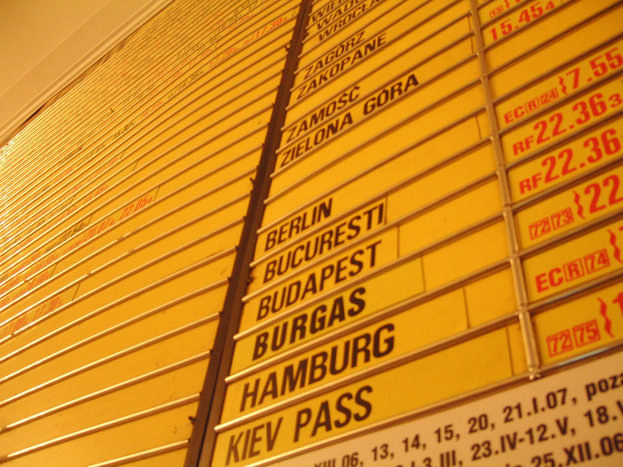 Eine gelbe Wand mit mehreren gelben Schildern, die wahrscheinlich Abfahrts- und Ankunftszeiten für verschiedene Ziele anzeigen.