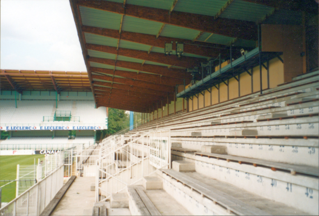 Alte Fotografie eines großen Stadions mit Sitzreihen, Geländern, Treppen, einem kleinen Schuppen, Informationsschildern, Rasenflächen, Bäumen und einem sichtbaren Himmel im Hintergrund.