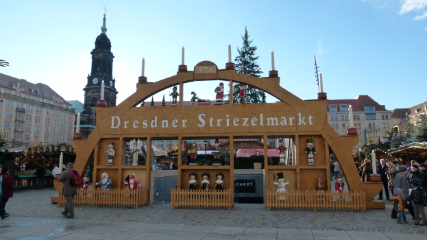 Ein geschäftiger Weihnachtsmarkt in Dresden, Deutschland mit Menschen, die spazieren gehen, einem Bogen, Bäumen, Gebäuden und einer bewölkten Himmel.