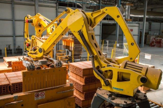 Großes Industriegebäude mit gestapelten Kisten, Kränen, Zäunen, Pfählen und einer fernen Wand in einer automatisierten Fertigungsumgebung.