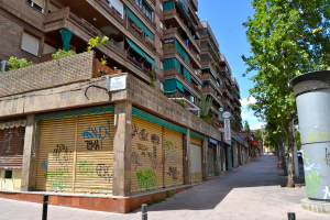 Eine Szene mit Gebäuden, Fenstern, grünen Kleidungsstücken, Geschäften, Schildern und umliegenden Bäumen und Pflanzen.