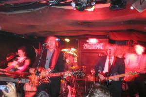 Eine Gruppe von Menschen singt auf der Bühne mit Gitarren und einem Mikrofon, während andere vorne Videos aufnehmen.