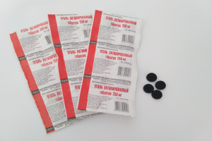 Drei Packungen schwarze Pillen auf einem weißen Tisch mit verstreuten schwarzen Gegenständen und Text auf den Packungen.