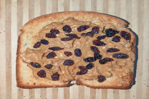 Ein Brotscheibe mit Erdnussbutter und Rosinen auf einer hölzernen Oberfläche.