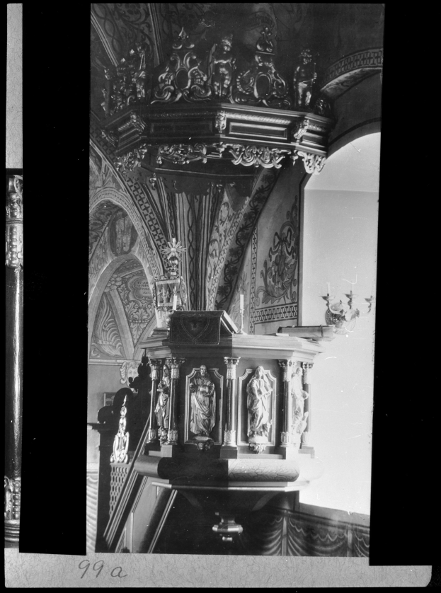 Ein Schwarz-Weiß-Foto eines Kirchenpults mit geschnitzten Säulen und einer strukturierten Wand im Hintergrund, mit Text am unteren Rand.