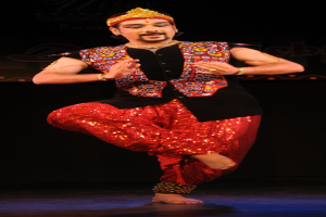 Ein Mann in roter und schwarzer Kleidung tanzt auf der Bühne, sein Gesicht ist zu sehen, die Augen geschlossen und der Mund leicht geöffnet.