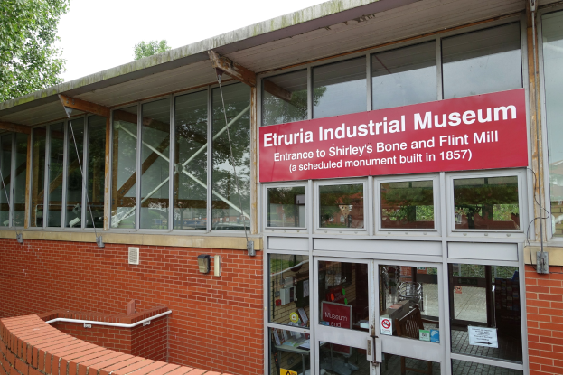 Außenansicht des Etruria-Industriemuseums mit Glaswänden, einem Textschild, einer Backsteinwand, einem Geländer, Bäumen und einem klaren blauen Himmel.
