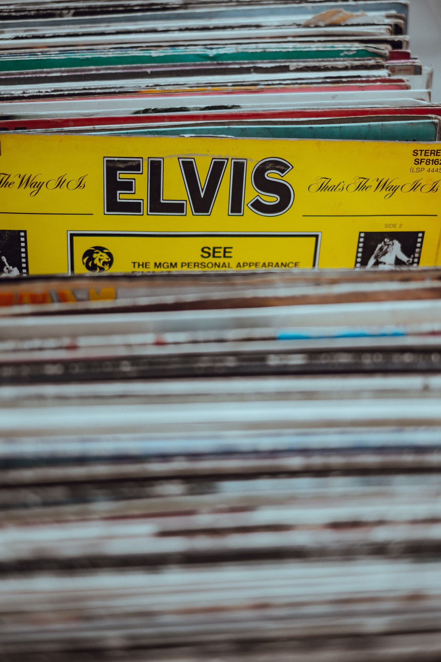 Ein ordentlicher Stapel von Elvis Presley-Platten auf einem Tisch, mit einigen Platten, die übereinanderliegen und Titel sichtbar sind, vor einem leicht unscharfen Hintergrund.