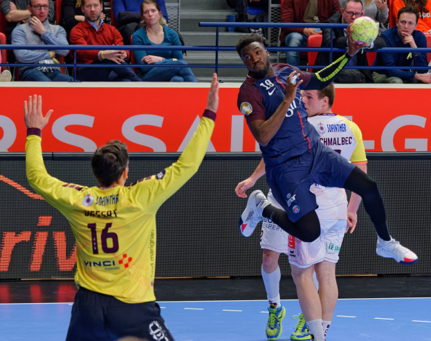 Mannengruppe spielt Handball auf einem Court mit einem Ball in der Luft in einer Stadionatmosphäre mit Zuschauern und einer Tafel, die "Futsal-Weltmeisterschaft 2019 - Paris Saint-Germain vs Bordeaux" anzeigt.