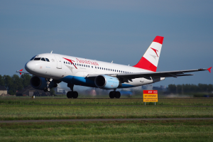 Ein Airbus A320-200 der Austrian Airlines startet vom Frankfurter Flughafen, mit einem Schild im Vordergrund, Gras, Bäumen, Gebäuden und einem klaren blauen Himmel im Hintergrund.