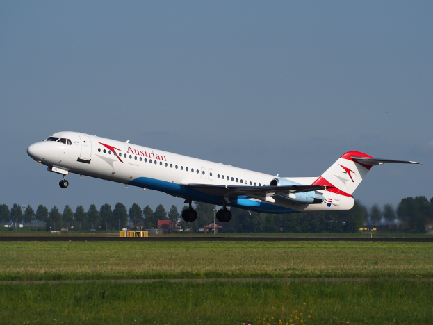 Austrian Airlines Embraer ERJ-190 Flugzeug beim Abheben vom Frankfurt Airport, mit grünem Gras, Bäumen, Gebäuden und Himmel im Hintergrund.