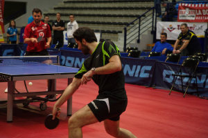 Eine Gruppe von Menschen in verschiedenen Farben, darunter schwarz, weiß und blau, versammelt sich um einen Tisch mit einem im Gange befindlichen Spiel, mit Stühlen und einer Treppe im Hintergrund.