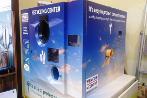 Blaues Recyclingzentrum mit "Recyclingzentrum"-Schild in der Mitte, einem Gestell mit Gegenständen links, einem einzelnen Gegenstand auf dem Boden rechts und Hintergrundbeleuchtung und Wand.