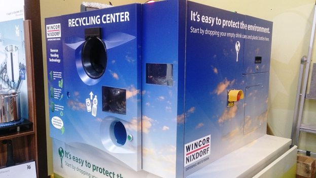 Blaues Recyclingzentrum mit "Recyclingzentrum"-Schild in der Mitte, einem Gestell mit Gegenständen links, einem einzelnen Gegenstand auf dem Boden rechts und Hintergrundbeleuchtung und Wand.