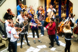 Eine Gruppe von Menschen, die Geigen spielen, mit verstreuten Papieren auf dem Boden.